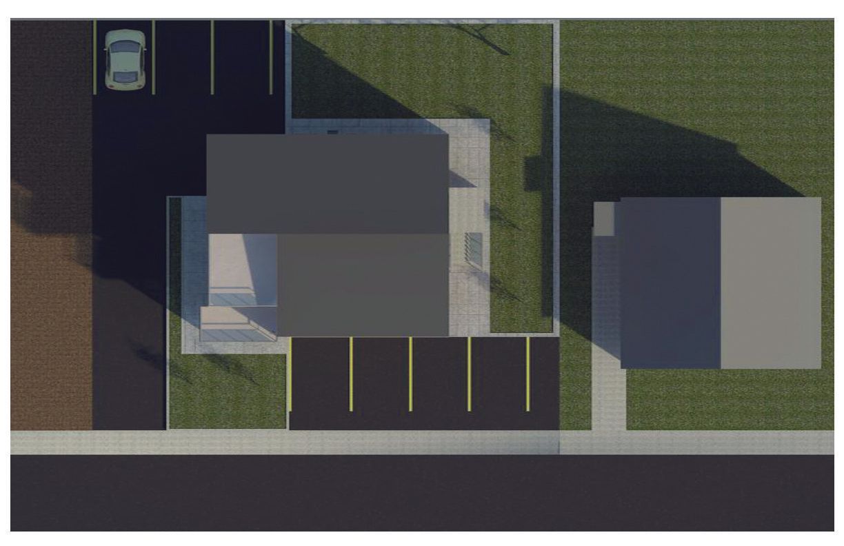 An aerial view showing two buildings, a parking lot, green lawn spaces, and a sidewalk along a road.