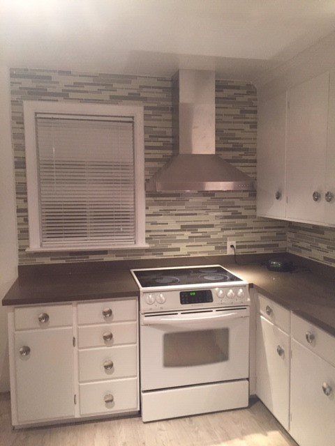 A kitchen featuring white cabinets, dark countertops, a white electric stove, a stainless steel hood, and mosaic tile.