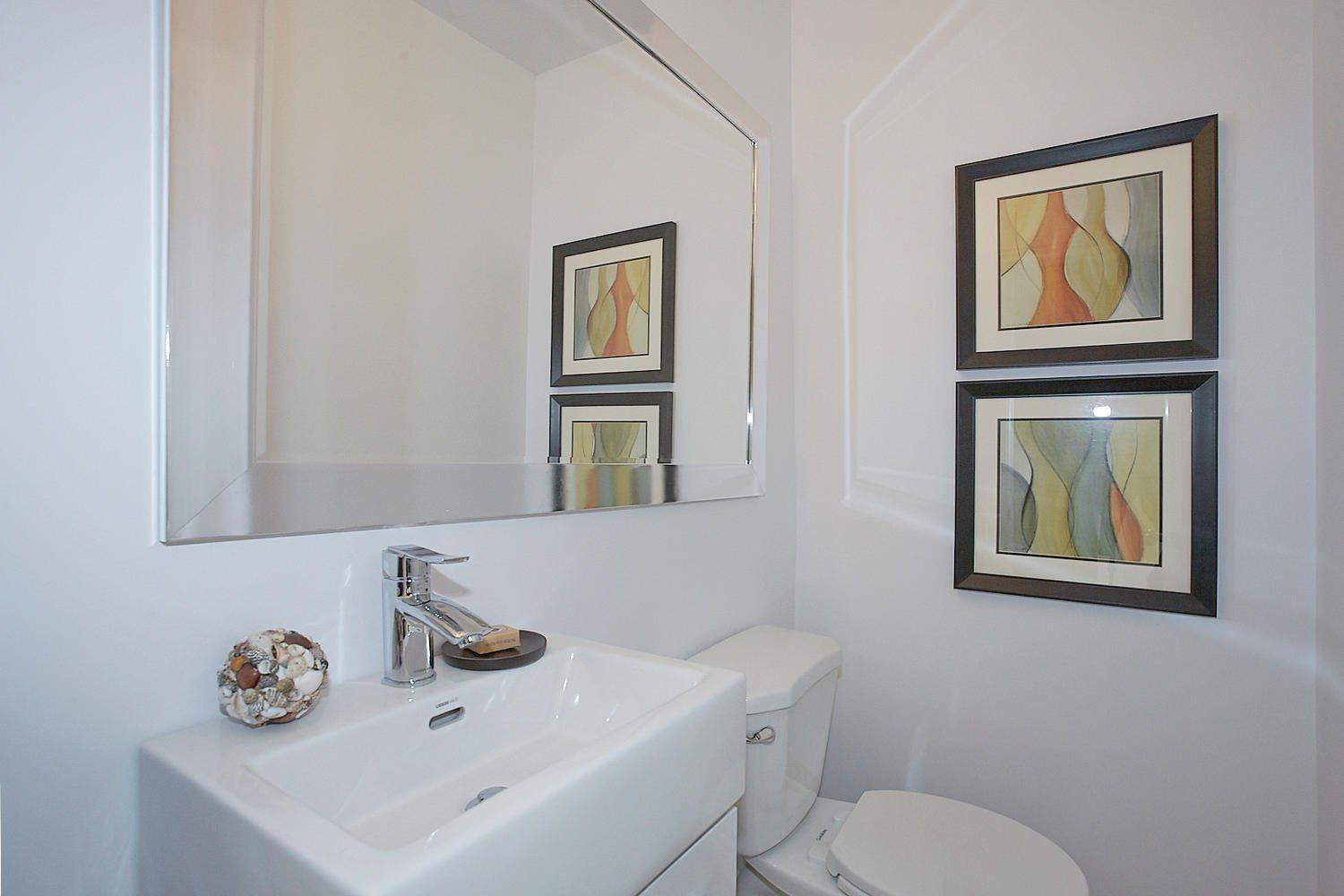 A white powder room featuring a floating sink, a large rectangular mirror, and two framed abstract art pieces on the wall.