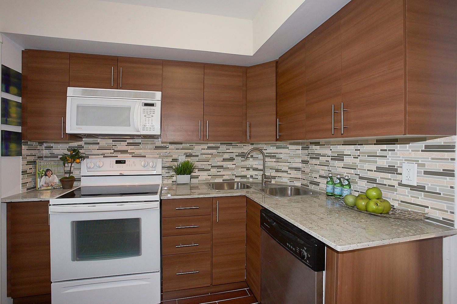 A kitchen with brown wood cabinets, white appliances, a stone tile backsplash, and light speckled granite countertops.