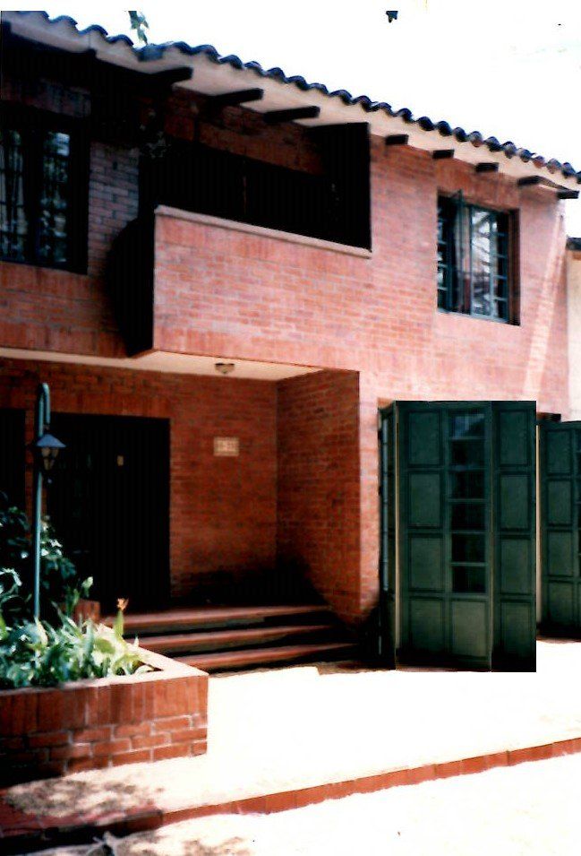A two-story red brick house with a tiled roof, dark wood accents, green shutters, and a front entry with steps.