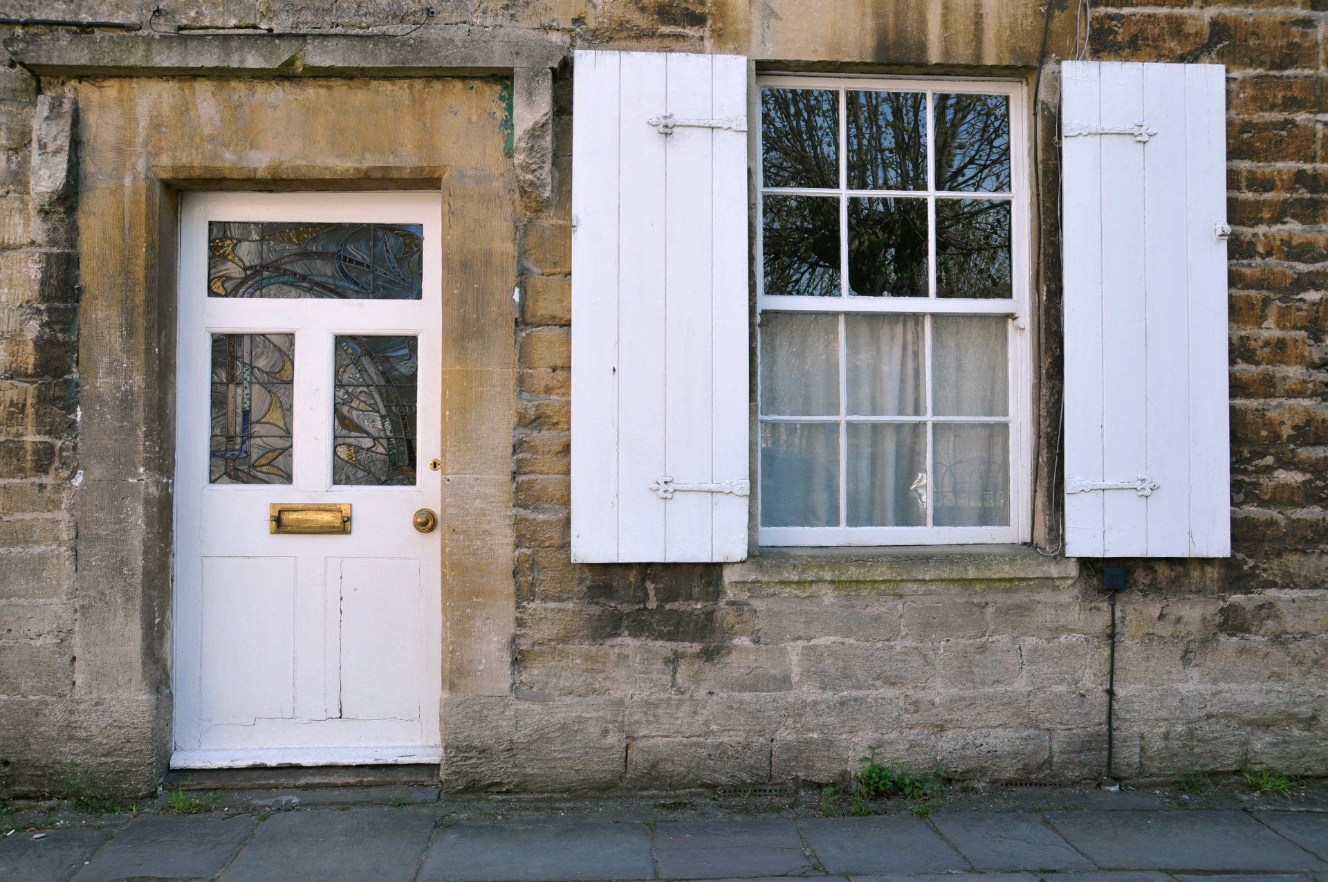 A white door and window with white shutters on a brick building