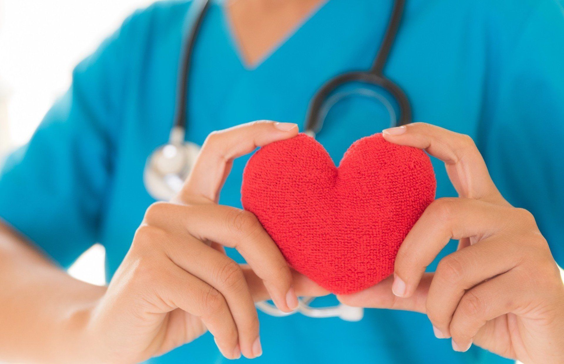 Nurse holding a red heart. She wears a blue scrub top and has a stethoscope around her neck.
