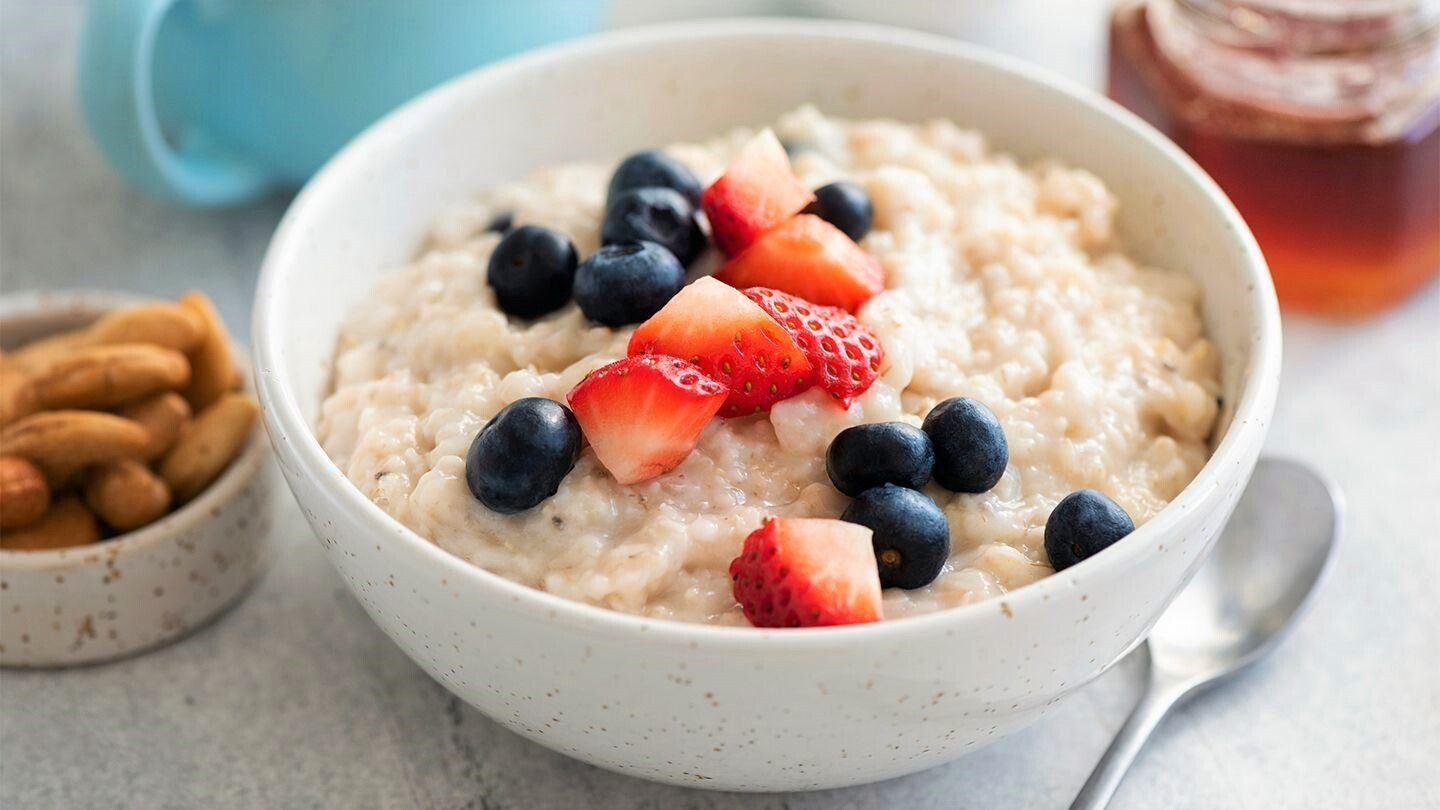 Bowl of oatmeal topped with blueberries and sliced strawberries, served with almonds and honey.