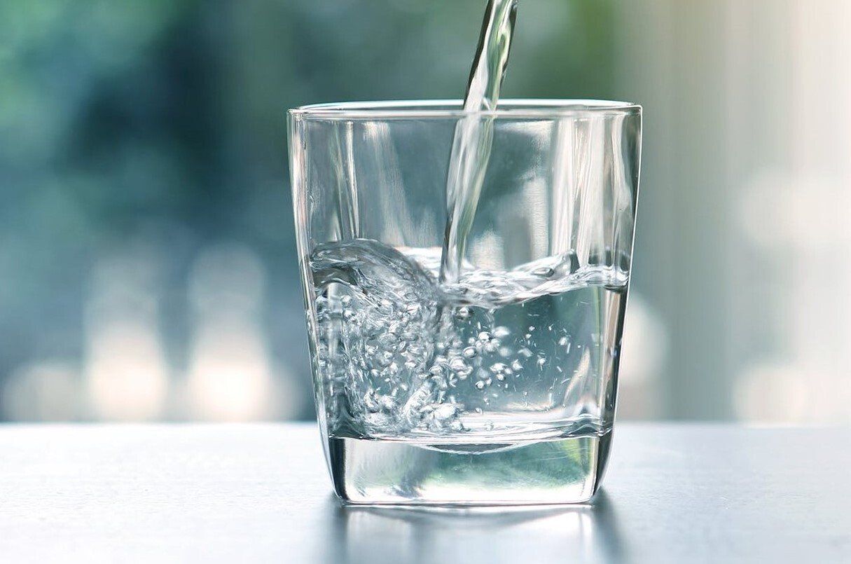 A glass being filled with clear water, blurred outdoor background.