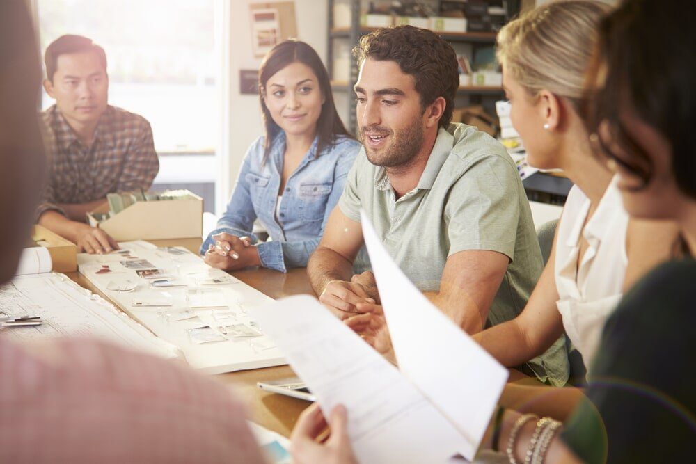 A Group Of People Are Sitting Around A Table Having A Meeting — Lynams Landscapes Pty Ltd in Cosgrove, QLD