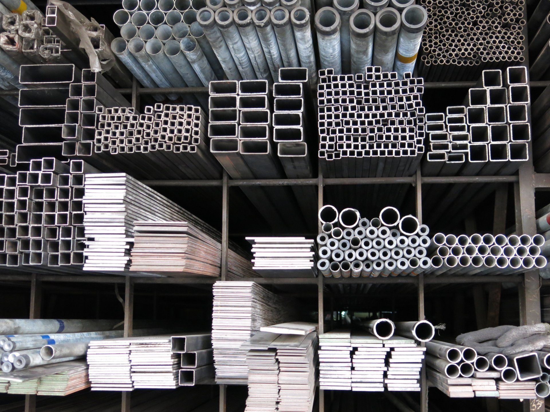 Tubi e barre metalliche di varie forme e dimensioni impilati sugli scaffali.