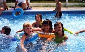 Children playing in a swimming pool, splashing and smiling with colorful float rings
