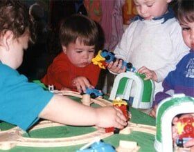 Children playing - Happy Hours Children's Center in Wappingers Fallas, NY Children playing with a toy train set at a table, reaching and concentrating on the tracks