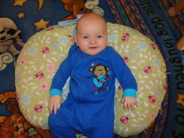 Smiling baby in blue onesie лежинг on a yellow patterned pillow