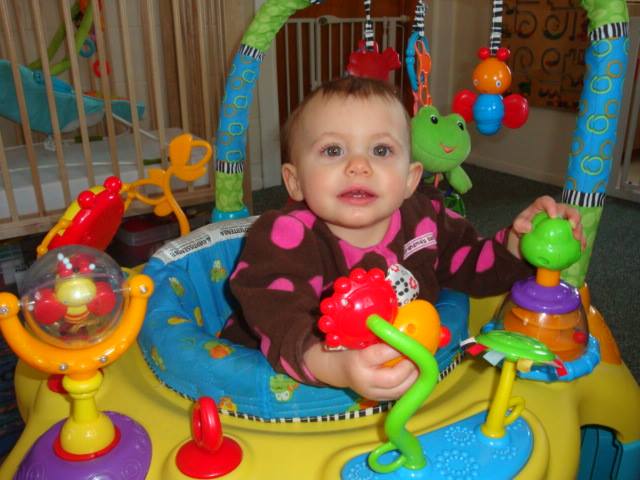 Baby sitting in a colorful activity center, smiling and reaching for toys.