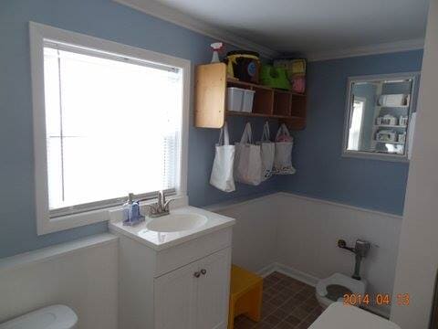 Small bathroom with sink, window, wall shelf, mirror, and blue-gray walls.