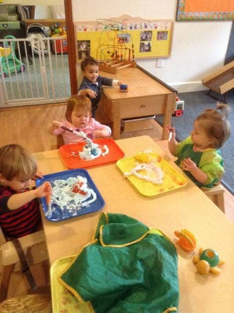 Children eating at a daycare table with colorful trays and toys nearby