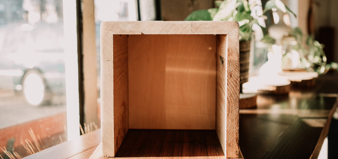 An empty wooden box is sitting on a wooden table in front of a window.