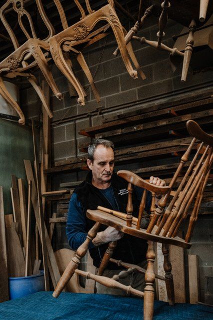 A man is working on a wooden chair in a workshop.