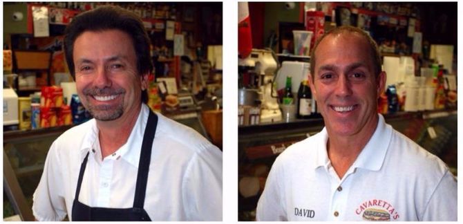 Two smiling men in white shirts standing in a shop interior
