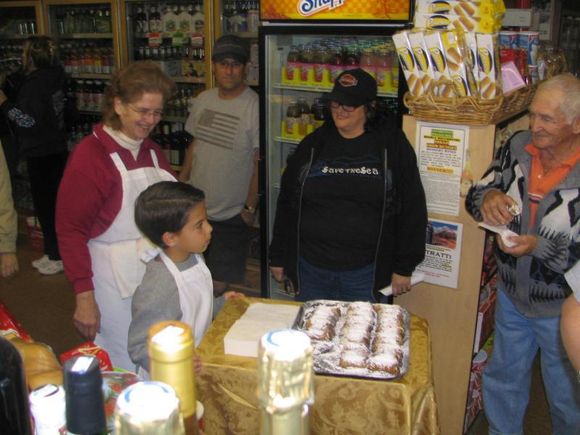 People gathered around a table with a cake in a small shop, smiling and chatting.