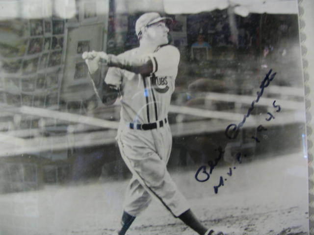 Black-and-white photo of a baseball batter swinging a bat with an autograph on the right