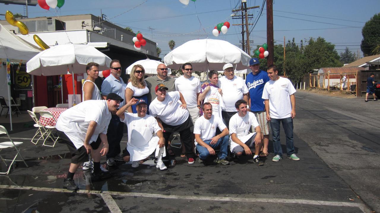 Group posing outdoors in white shirts beside a street, with umbrellas and colorful balloons in the background.