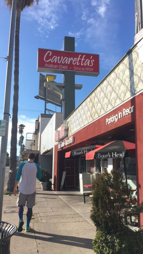 Sunny street with red storefront signs, a pedestrian walking, and blue sky overhead.