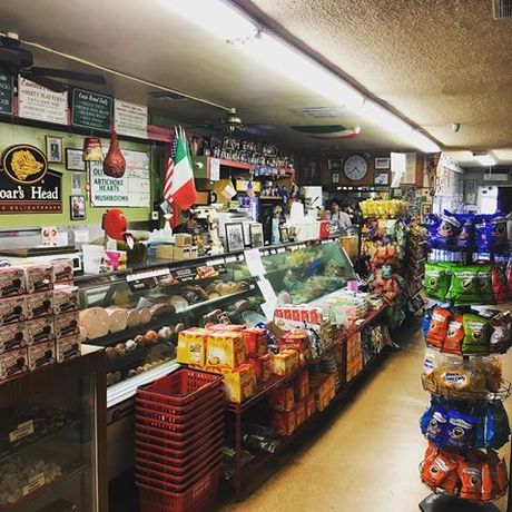 A cozy deli/grocery store aisle with shelves of snacks, meats, and drinks under warm lighting.