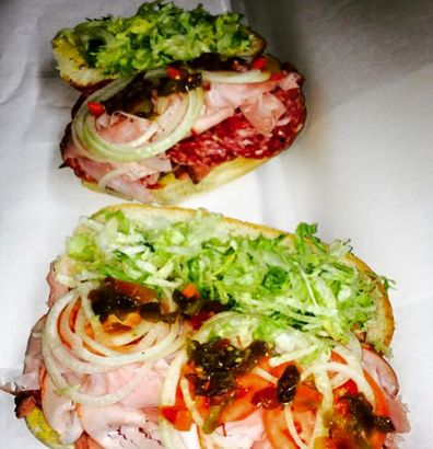Two open-faced sandwiches with shredded lettuce, onion, and tomato on white parchment.