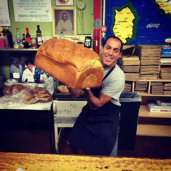 Bakery worker smiling and holding a giant loaf of bread at the counter