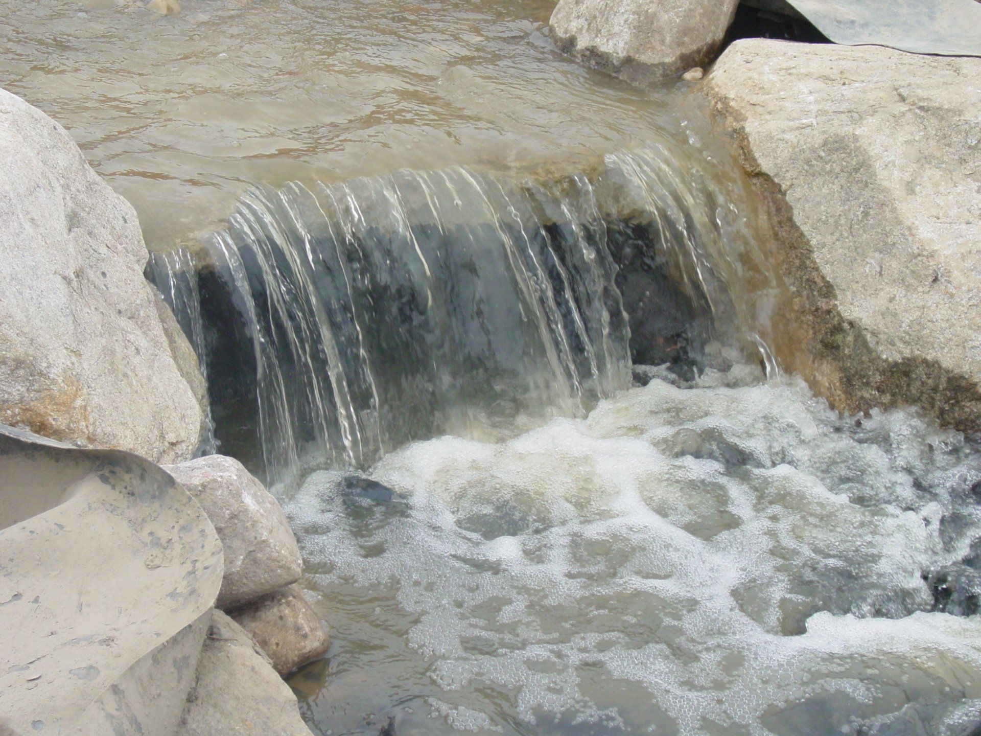 A small waterfall is surrounded by rocks and foamy water