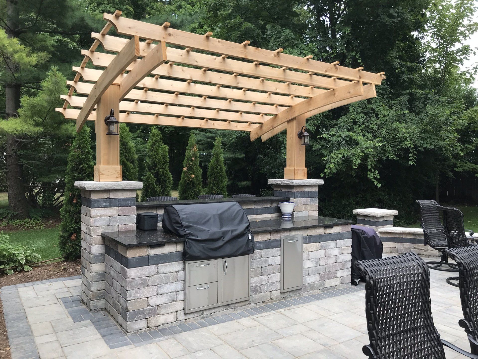 An outdoor kitchen with a grill under a wooden pergola.