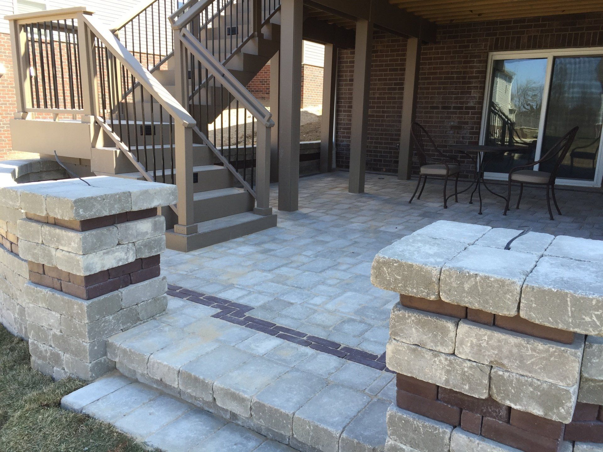 A patio with stairs leading up to a deck and a table and chairs.