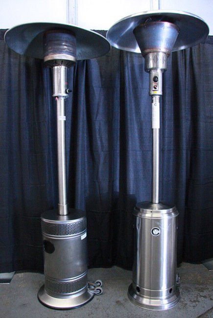 Two silver patio heaters standing side by side in front of dark curtains