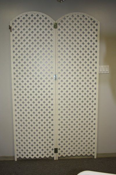 White lattice folding screen standing against a beige wall in a carpeted room