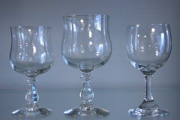 Three empty clear stemmed glasses on a gray surface