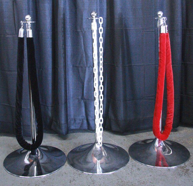 Three velvet rope stanchions: black, white chain, and red, on round metal bases indoors