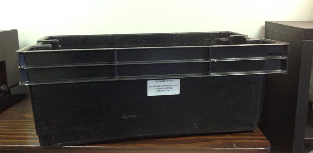 Black plastic storage tote with lid on a table against a light wall