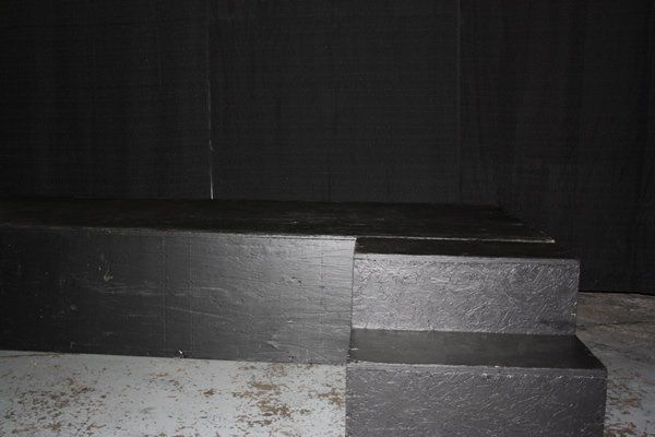 Dark stage steps with a black backdrop and concrete floor in front
