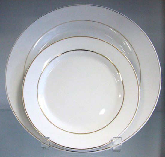 Stacked white plates with gold rims on a gray surface