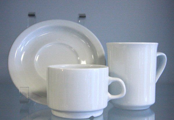 White cup and saucer with a white mug on a reflective surface, shown against a gray background