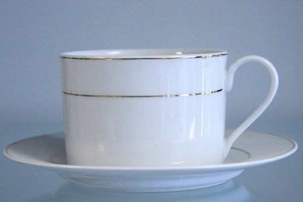 White teacup with gold rim on a matching saucer against a pale blue background
