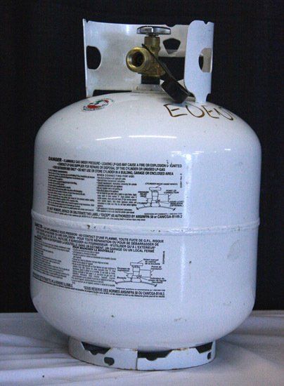 White propane tank with brass valve and printed labels on a gray surface