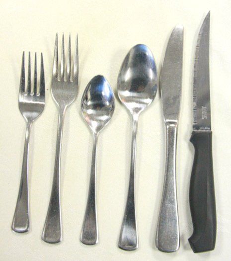 Six silverware pieces—forks, spoons, and knives—lined up on a white surface.
