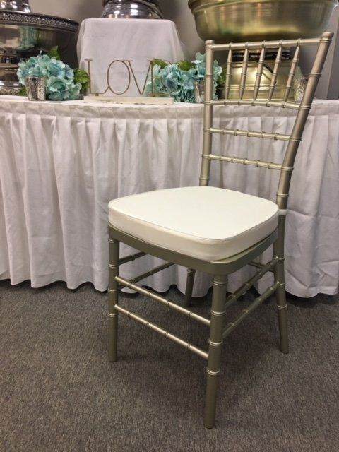 Gold Chiavari chair with white cushion beside a decorated table with a white skirting cloth and floral accents.