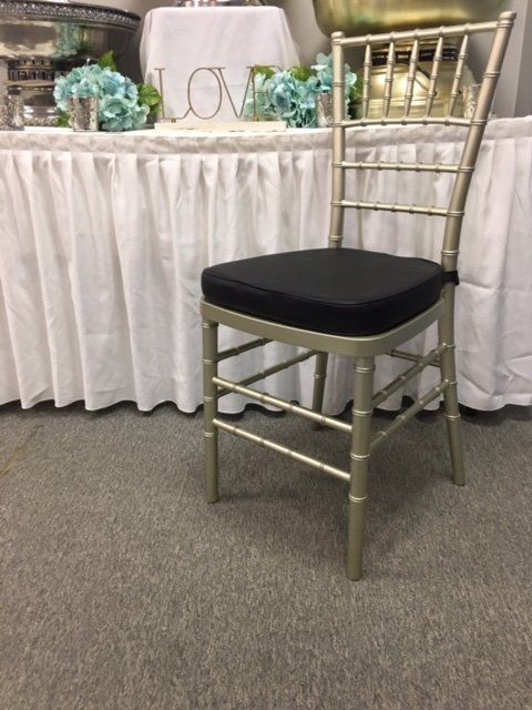 Gold chiavari chair with black cushion in front of a decorated banquet table