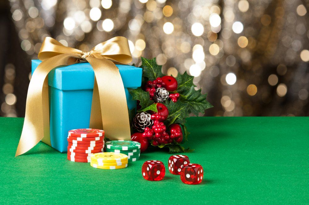 Christmas gift box with gold ribbon, candy, and red berries on a green table