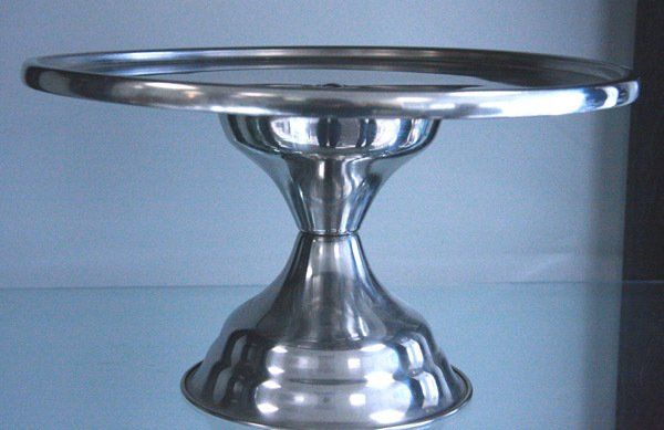 Silver metal pedestal cake stand on a reflective surface, shown against a plain background