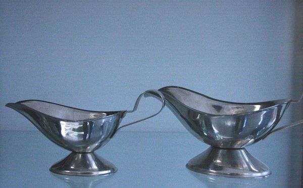 Two silver gravy boats linked by a handle, sitting on a blue surface