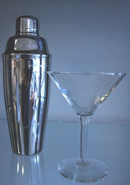 A silver cocktail shaker beside a clear martini glass on a reflective surface