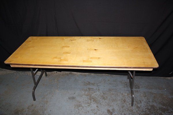 Wooden folding table with metal legs on a concrete floor against a dark backdrop