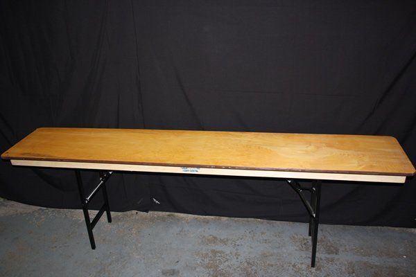 Long wooden folding table with black metal legs against a dark backdrop.