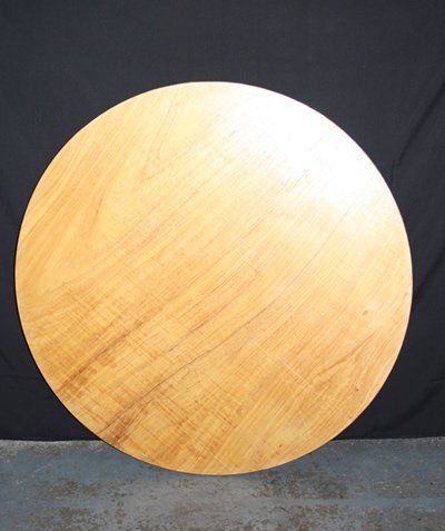 Large round wooden tabletop leaning against a black backdrop on a gray floor.